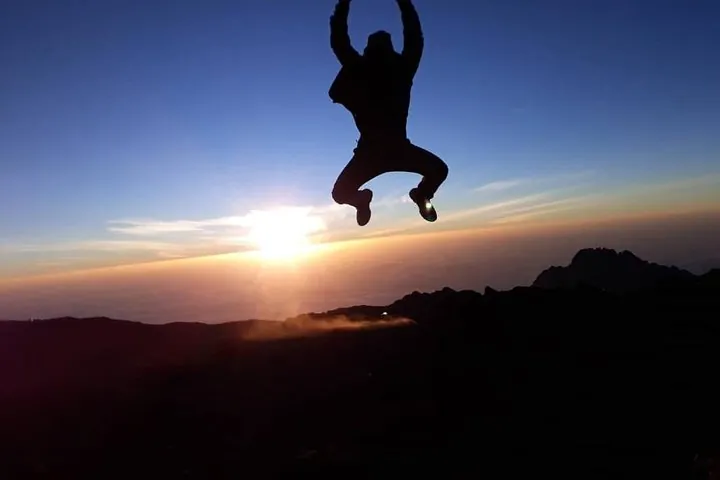 Climber jumping in silhouette at sunrise on a Kilimanjaro climbing tour by the Machame Route, Tanzania