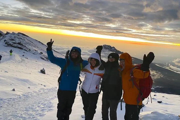 Four climbers in the snow above the clouds at sunrise on a Kilimanjaro climbing tour by the Lemosho Route, Tanzania