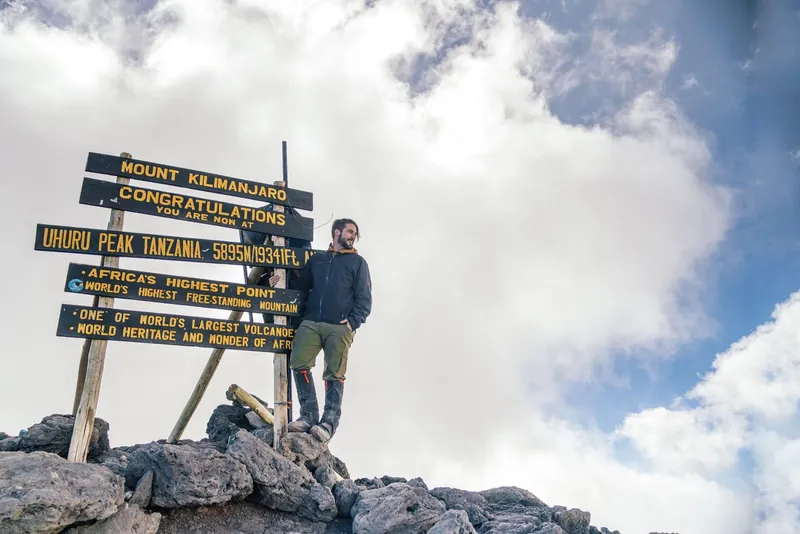 Climber beside the Uhuru Peak sign under cloud on a Kilimanjaro climbing tour by the Marangu Route, Tanzania