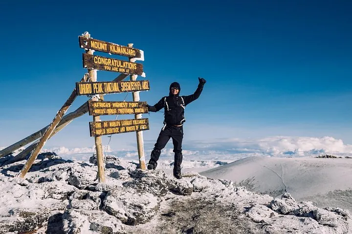 Climber with raised arms at the Uhuru Peak sign on a Kilimanjaro climbing tour by the Northern Circuit, Tanzania